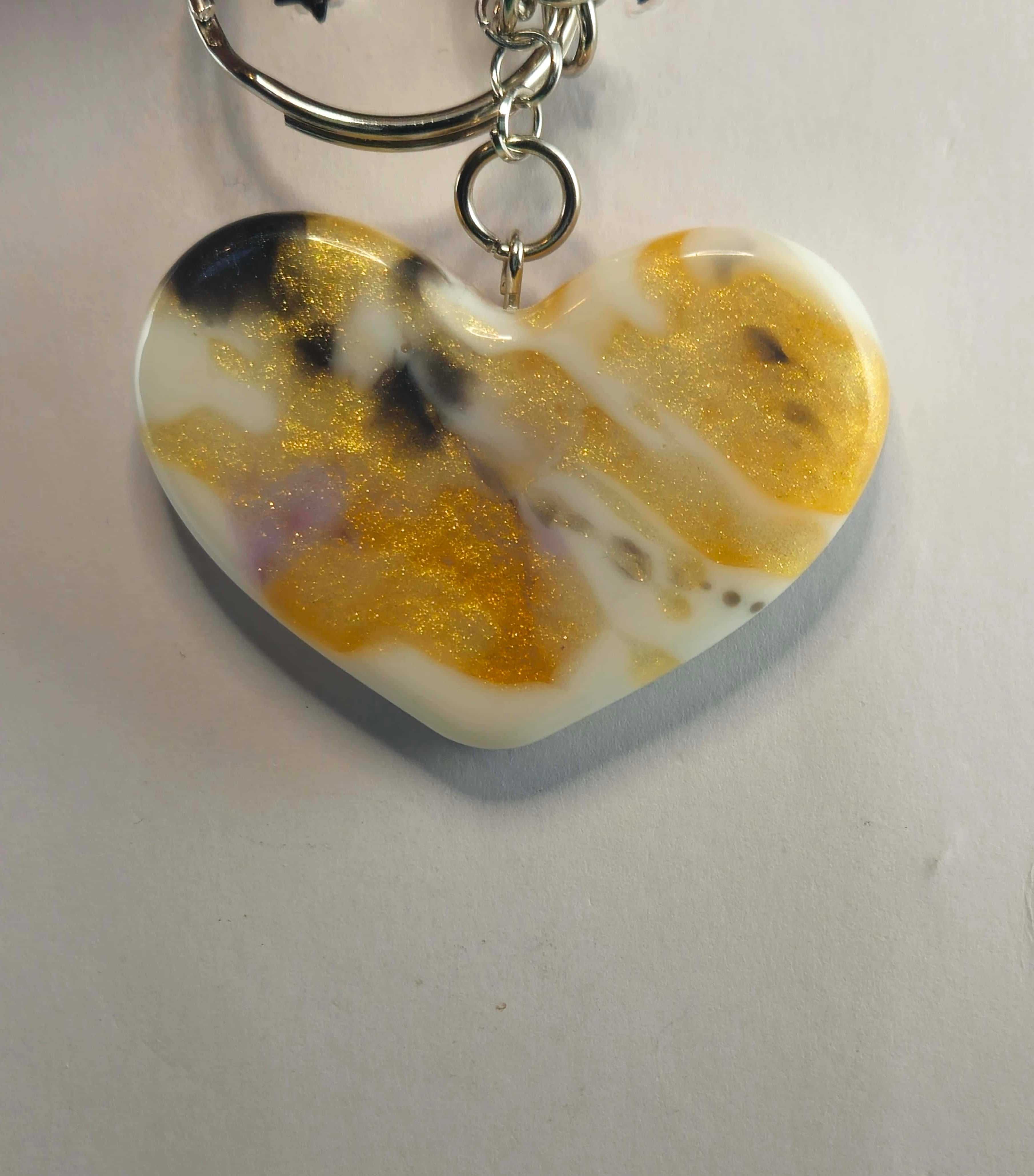 Heart-shaped resin keychain with gold, black, and white swirls and glitter accents