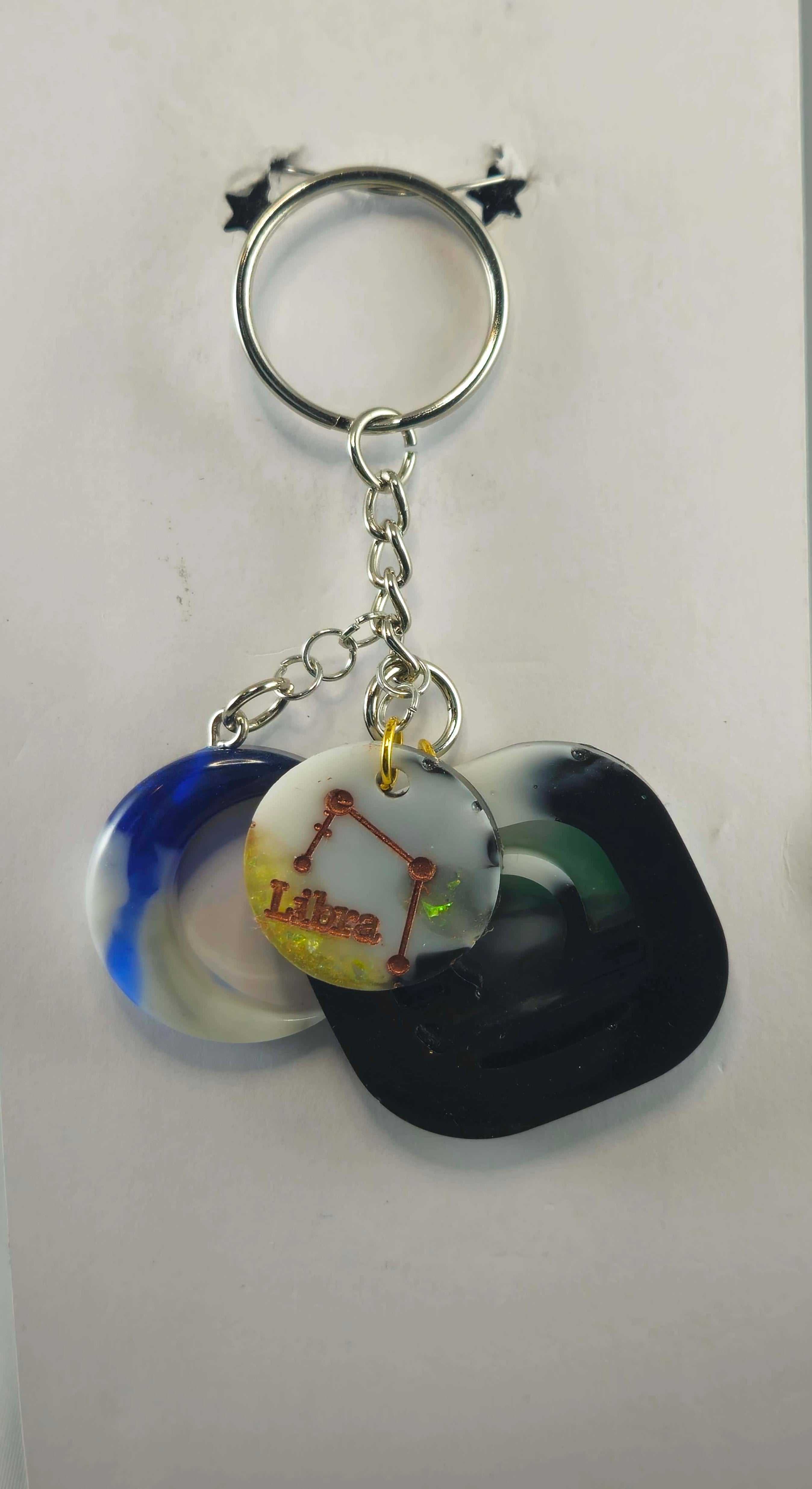 Metal keychain with zodiac-themed charms, including a Libra clock face and colorful resin shapes
